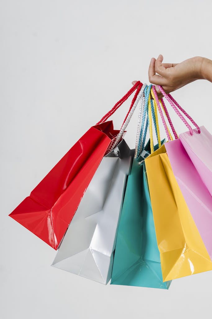 Close-up of a hand holding multiple colorful shopping bags on a white backdrop, perfect for retail or consumerism concepts.